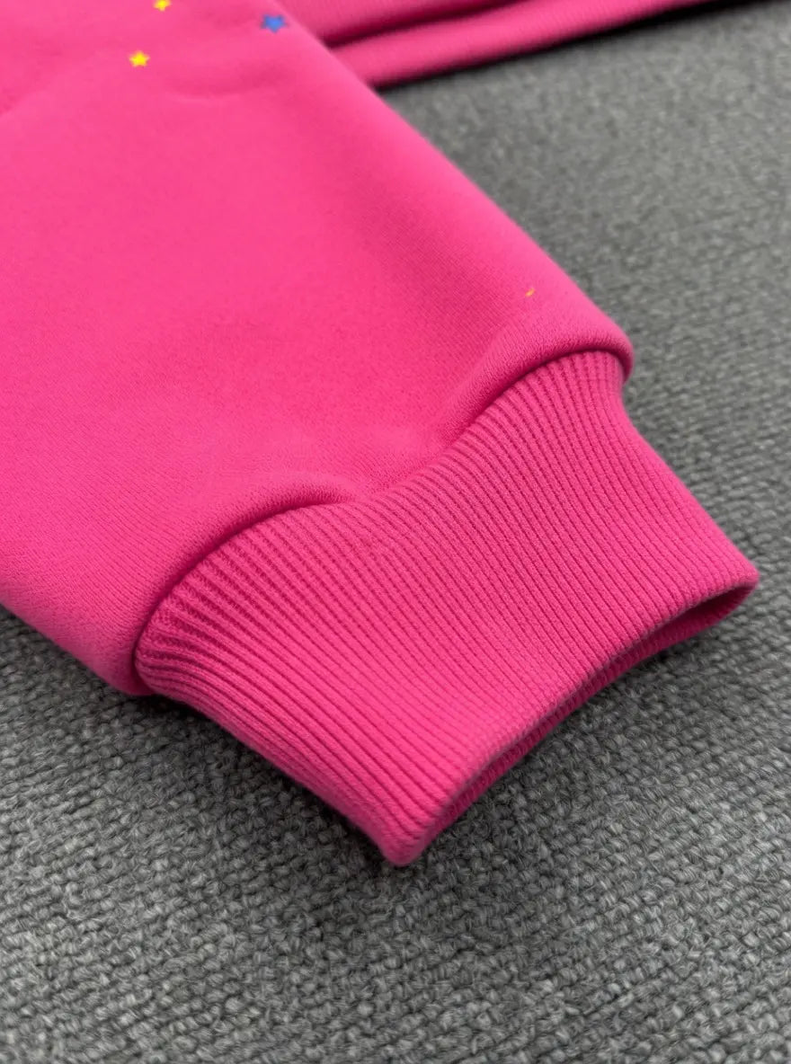 Close-up of the Sp5der 555 Web Pink Hoodie Streetwear Pullover’s bright pink sleeve with ribbed cuff, set on a textured gray surface, reflecting its bold streetwear style.