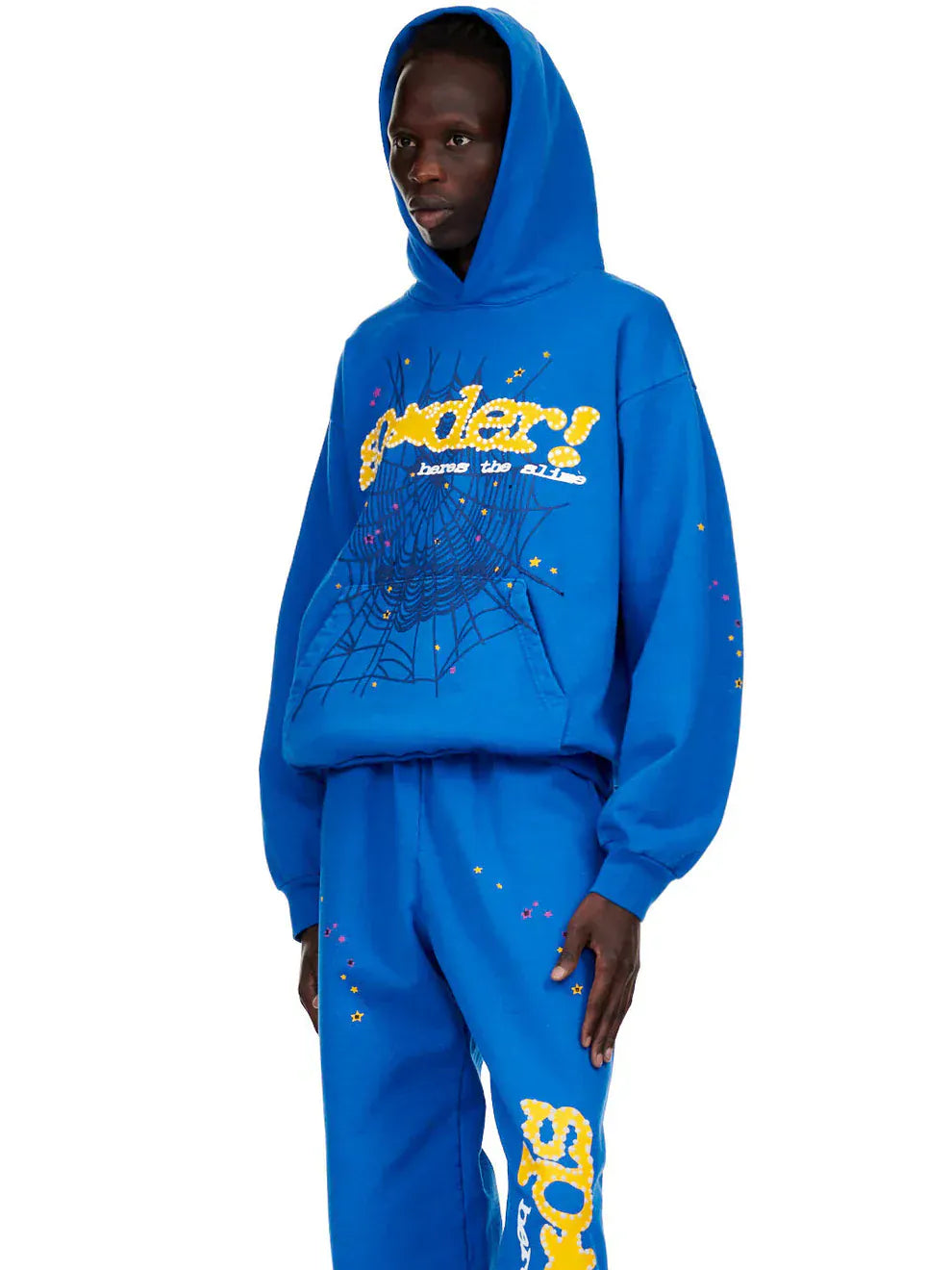 Someone wears the Sp5der “Hares the Slime” Hoodie (440GSM) in royal blue, featuring a fuzzy logo and spider-web graphic—a standout heavyweight streetwear piece.