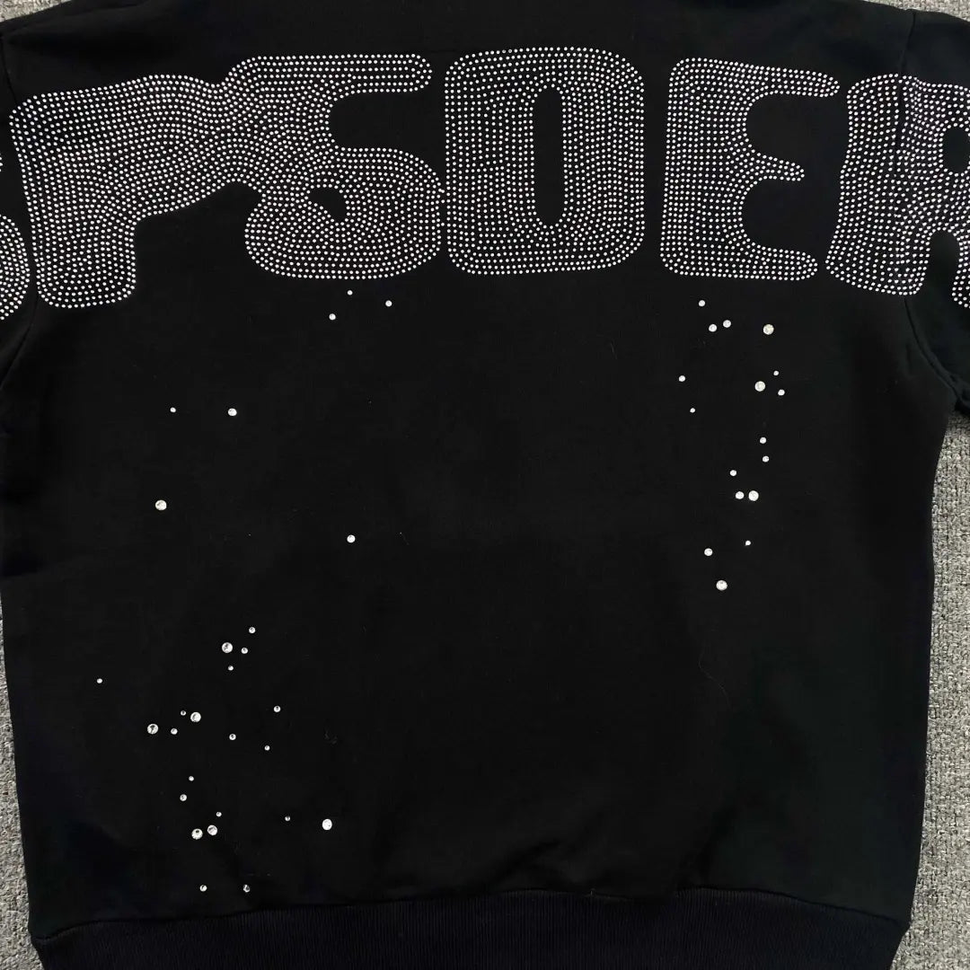 The Sp5der Black Rhinestone Spiderweb Crystal Hoodie features bold lettering with rhinestone outlines across the back and scattered crystals below, delivering a standout streetwear look.