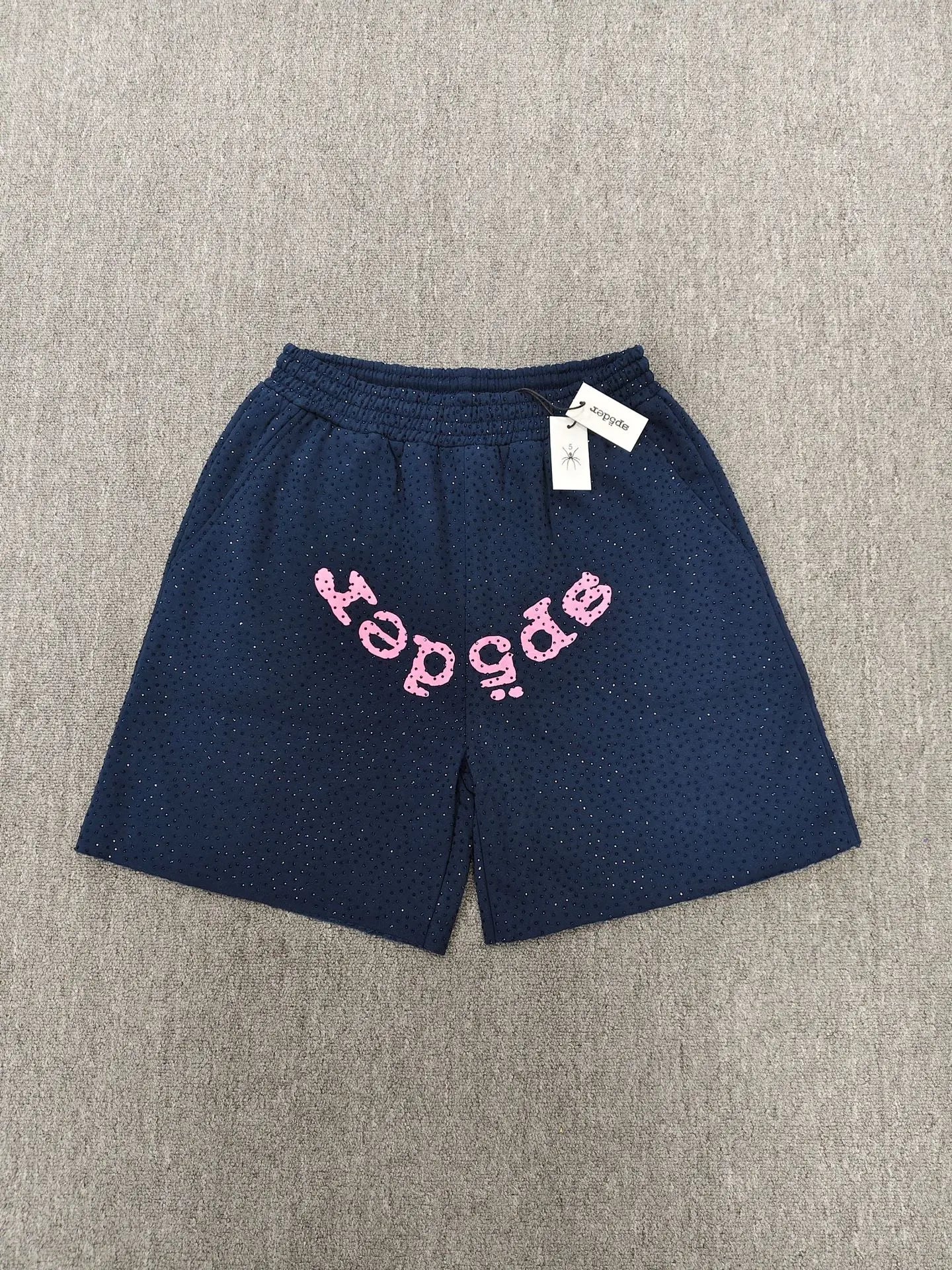 Navy Sp5der jogger shorts featuring a pink text graphic across the front and an elastic waistband.