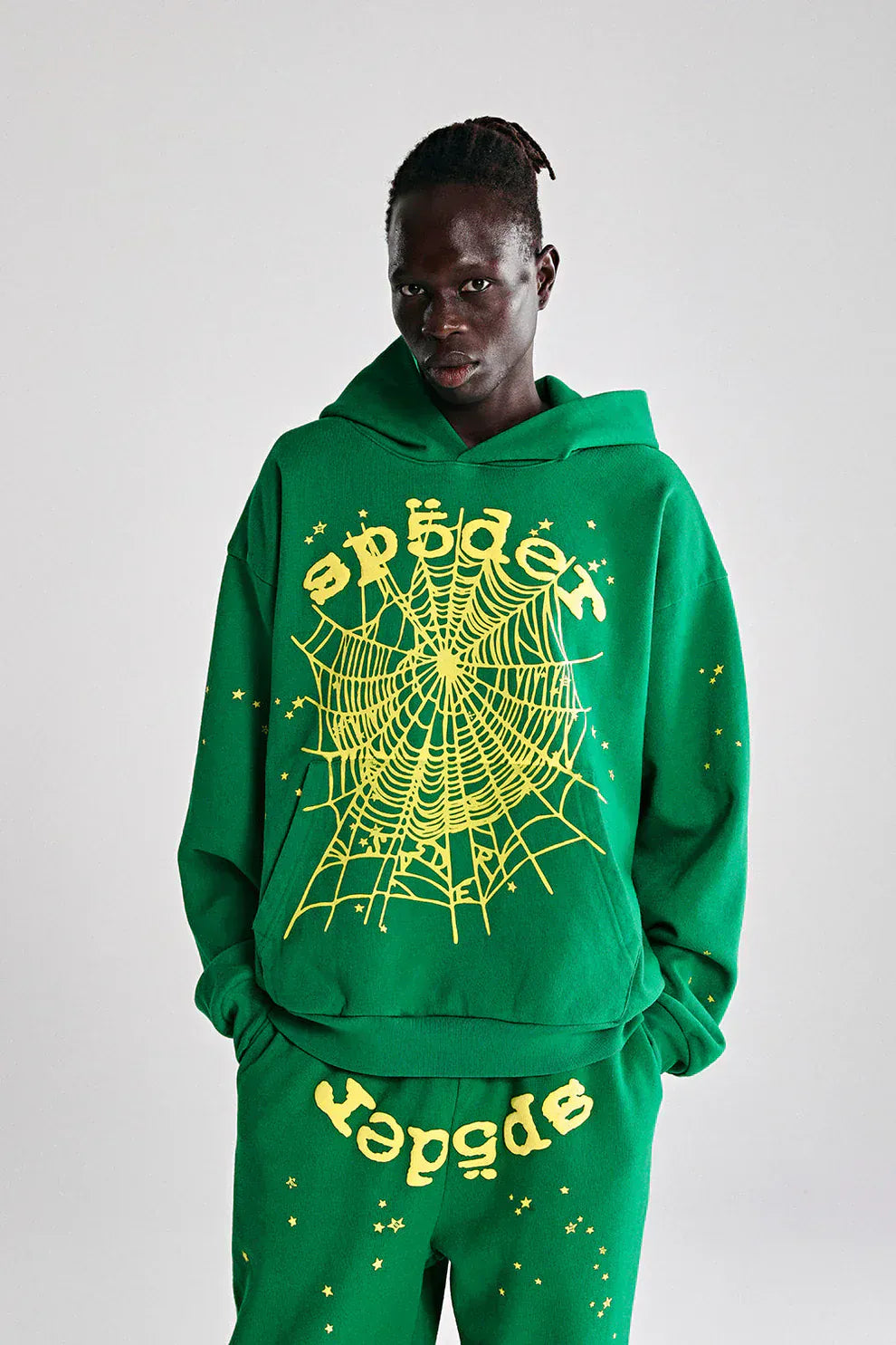 A person wears the Sp5der Web Hoodie – Emerald Green & Yellow 440GSM Heavyweight Oversized Streetwear Pullover with matching pants, both featuring yellow spider web designs and "sp5der" text, showcasing bold street style.
