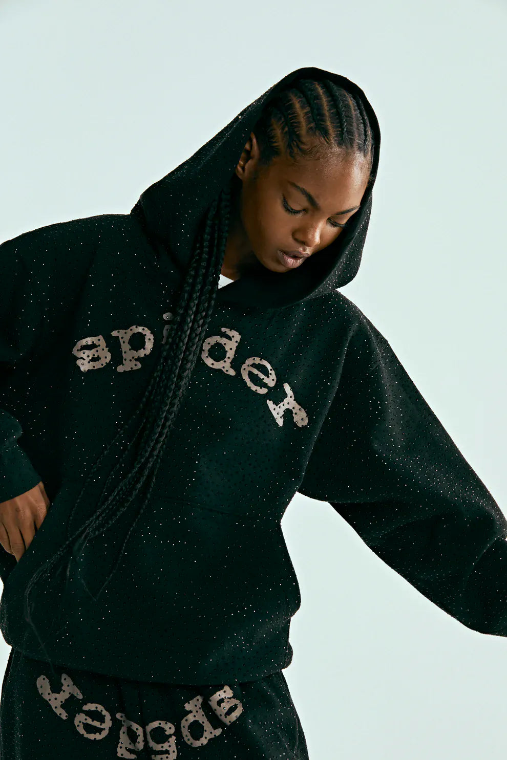 A person wearing the VVS Spider Hoodie – a black Sp5der rhinestone pullover with diamond graphic detail – and matching black sweatpants, standing against a plain light background.