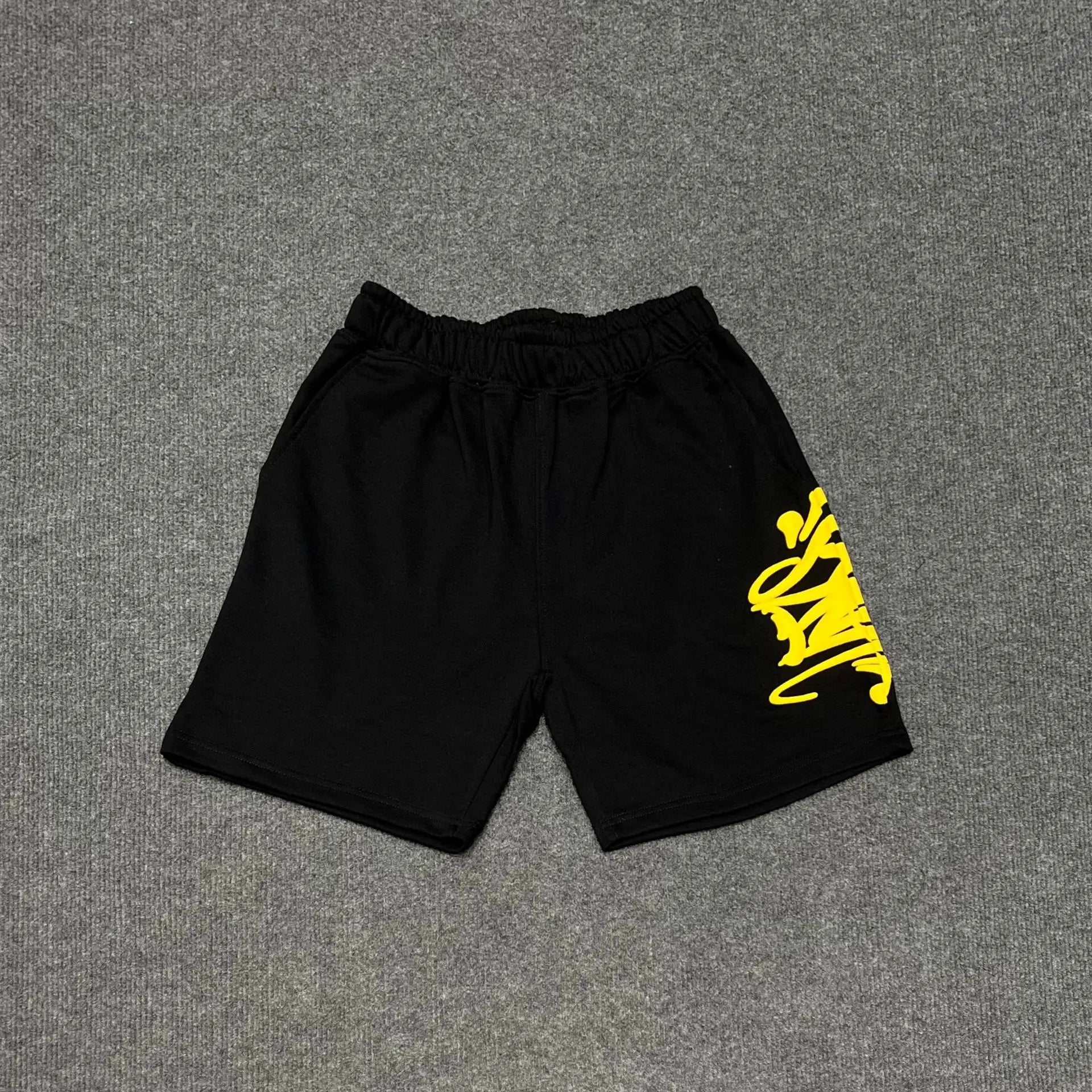 Black cotton jogger shorts with yellow graffiti letter print on the right leg and drawstring waistband