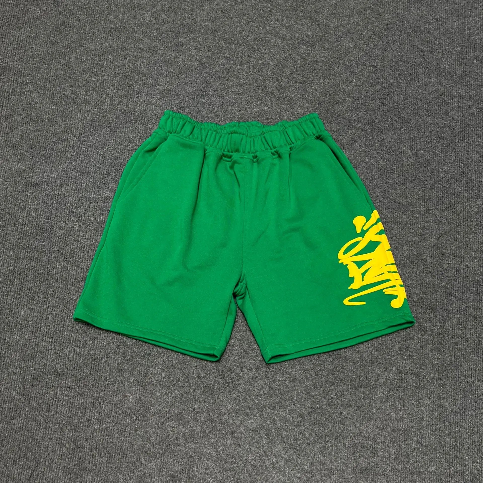 Green cotton jogger shorts with yellow graffiti graphic print on right leg and elastic drawstring waistband
